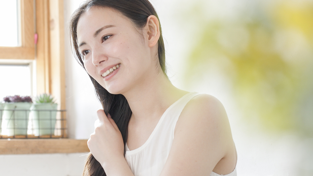 髪の毛を笑顔で触る女性